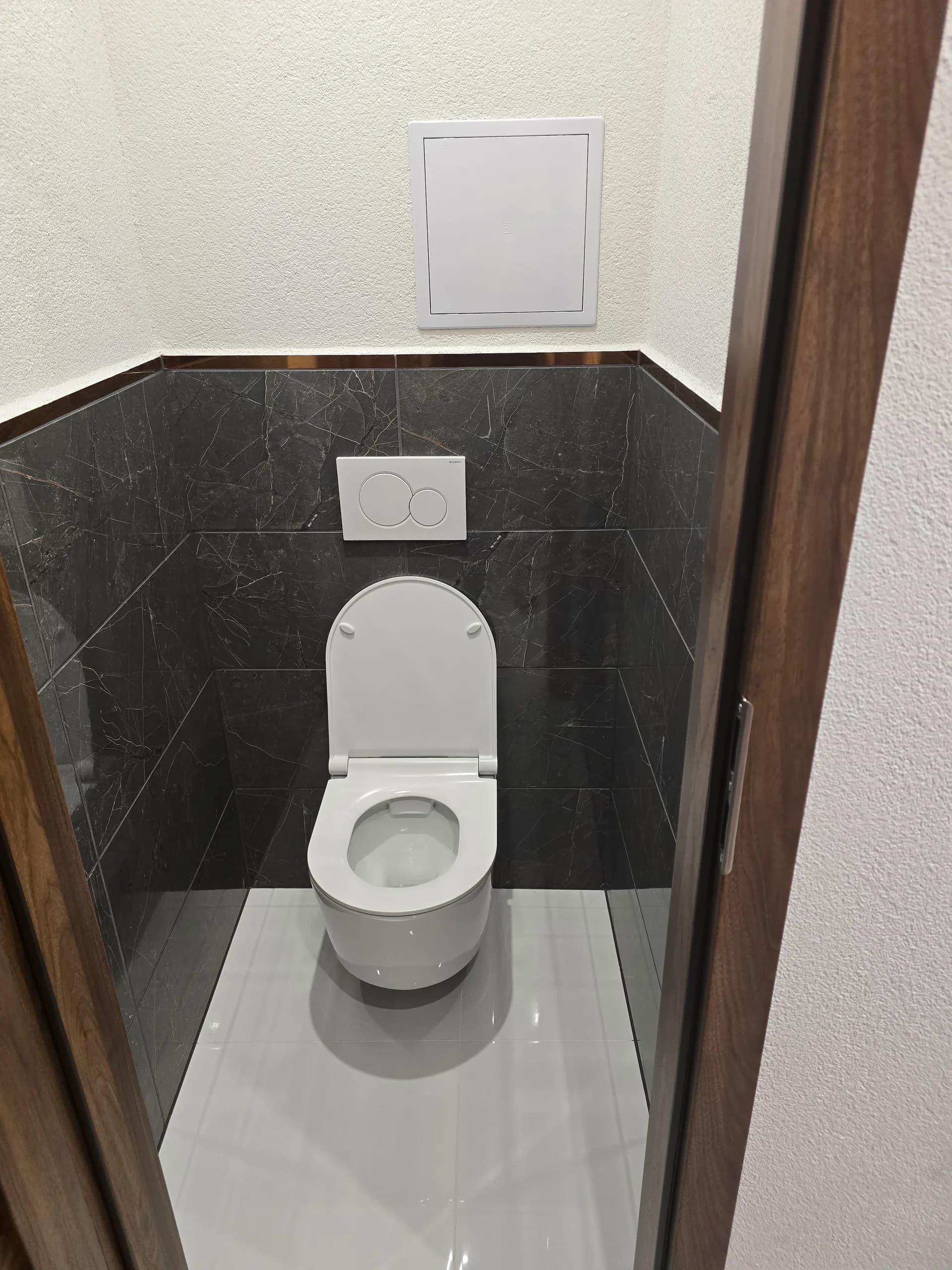 Samostatné WC so závesnou misou a obkladom v dekore tmavého mramoru