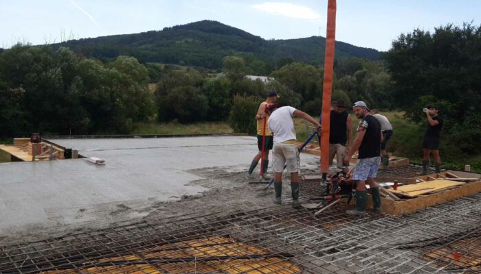 Pohľad na prebiehajúcu betonáž stropnej dosky, partia murárov vylieva a zrovnáva betón